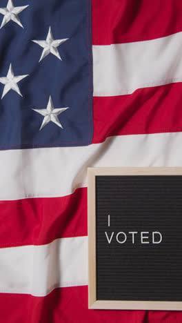 Vertical-Video-Of-Sign-Reading-I-Voted-Lying-On-US-Stars-And-Stripes-Flag-For-American-Election-2024-2